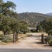 Rural Valley Center property with a dirt driveway, live oaks and dry chaparral hills in neutral daylight, illustrating a San Diego County murder case.