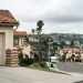 Sandbags stacked beside a garage door on a Southern California residential street under an overcast sky, with hillsides blurred in the background.