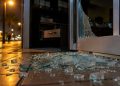Shattered glass pieces on the tile floor at the threshold of a restaurant's glass door at night in Arcadia, lit by a nearby street lamp.