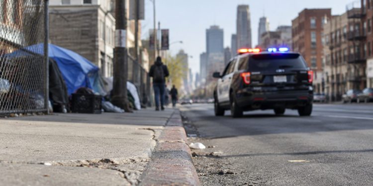 Skid Row street in downtown Los Angeles with brick buildings and chain-link fencing, street curb in sharp focus, patrol SUV further down, softly blurred.