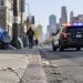 Skid Row street in downtown Los Angeles with brick buildings and chain-link fencing, street curb in sharp focus, patrol SUV further down, softly blurred.