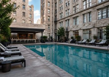 Small rectangular courtyard pool with lounge chairs between tall masonry walls of an older downtown Los Angeles hotel in neutral daylight.