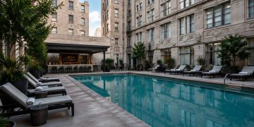 Small rectangular courtyard pool with lounge chairs between tall masonry walls of an older downtown Los Angeles hotel in neutral daylight.