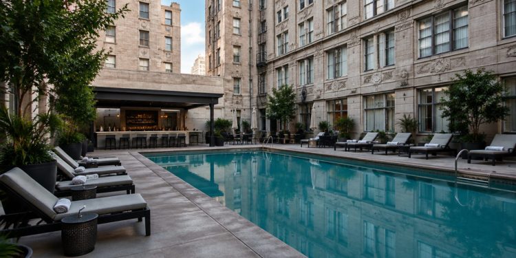 Small rectangular courtyard pool with lounge chairs between tall masonry walls of an older downtown Los Angeles hotel in neutral daylight.