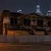 Soot-stained two-story commercial row with boarded openings and metal barriers on a downtown Los Angeles street at night under street lamps.