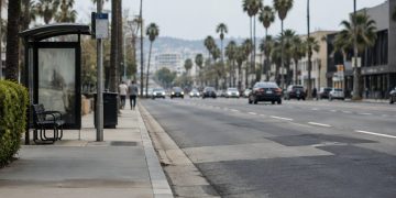 Sunset Boulevard in West Hollywood in neutral daylight, with a concrete bus pad beside patched asphalt, palm trees and low-rise buildings along the roadway.