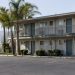 Two-story motel exterior in Los Angeles County with a second-floor walkway and small bathroom windows under neutral daylight, palm trees beside an empty lot.