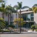 West Hollywood City Hall seen from across Santa Monica Boulevard in neutral daylight, with palm trees in the foreground, illustrating the city council race.