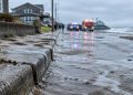 Wet sand and seawater cover a beachfront street on the Long Beach Peninsula, with a sodden curb in sharp focus and homes softly blurred in the background.