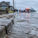Wet sand and seawater cover a beachfront street on the Long Beach Peninsula, with a sodden curb in sharp focus and homes softly blurred in the background.