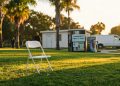 White folding chairs arranged on West Hollywood Park's Robertson Lawn in late afternoon, with vending machine and restroom building blurred in background.