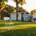 White folding chairs arranged on West Hollywood Park's Robertson Lawn in late afternoon, with vending machine and restroom building blurred in background.