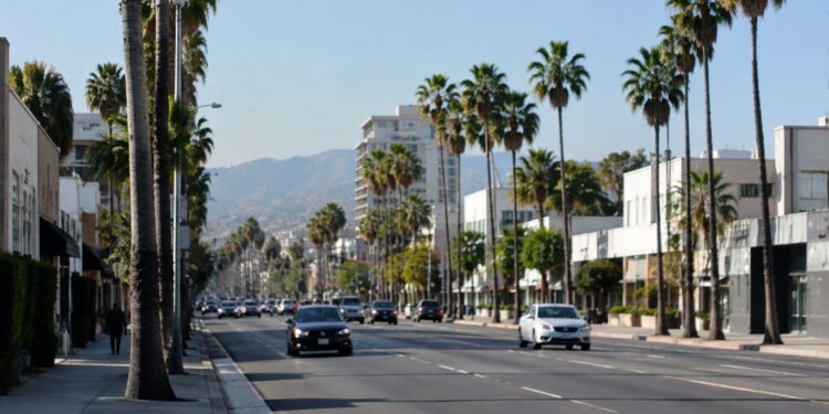 Wide daylight view of Santa Monica Boulevard in West Hollywood, with palm trees and low-rise commercial buildings along the busy corridor.