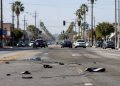 Wide view of a South Los Angeles intersection with vehicle debris scattered across the asphalt, low-rise storefronts and palm trees in morning daylight.