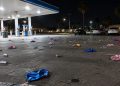 Wide view of a gas station parking lot at night in Bellflower, with small silver canisters and balloons scattered across the asphalt under canopy lights.