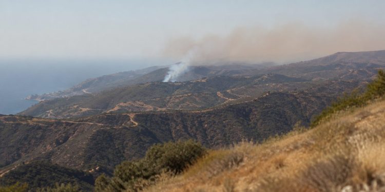 Wide view of dry chaparral ridgelines in the Santa Monica Mountains near Malibu with a thin plume of smoke rising over the hills in afternoon daylight.