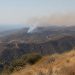 Wide view of dry chaparral ridgelines in the Santa Monica Mountains near Malibu with a thin plume of smoke rising over the hills in afternoon daylight.
